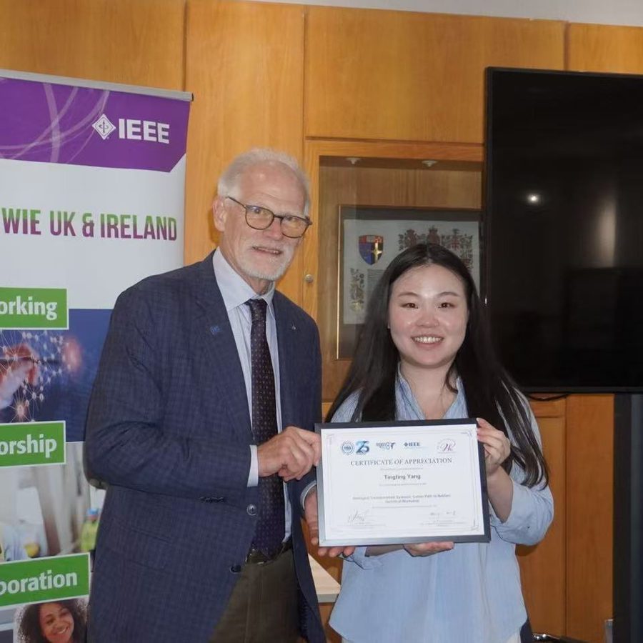Tingting Yang holding a certificate of appreciation next to a presenter, in front of an IEEE Women in Engineering UK and Ireland banner.