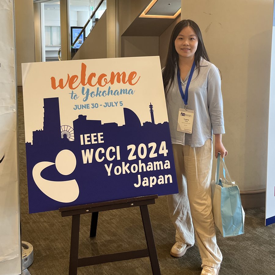 Tingting Yang standing beside the IEEE WCCI 2024 Yokohama welcome sign.